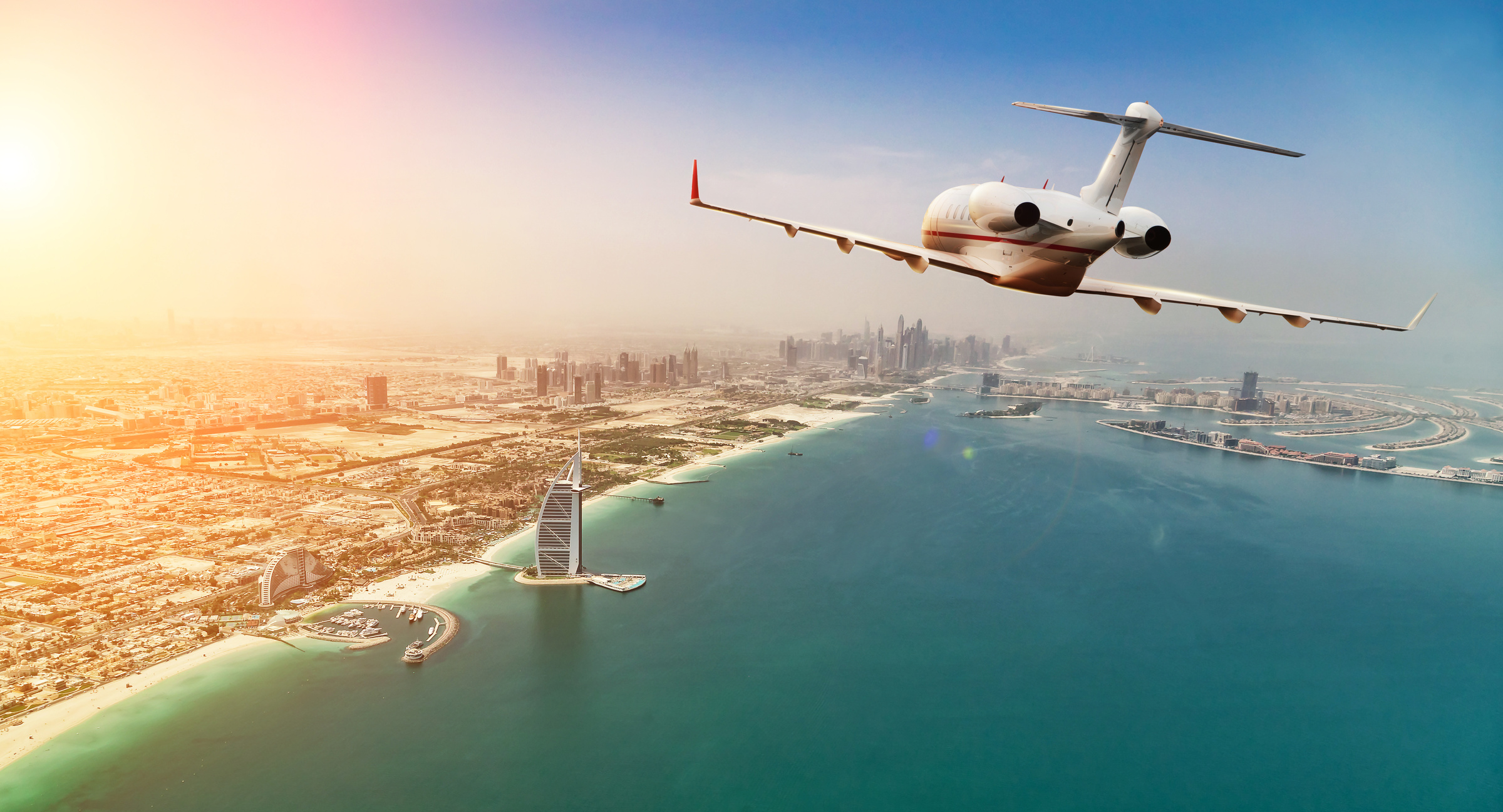 Private jet plane flying above Dubai city in beautiful sunset light.